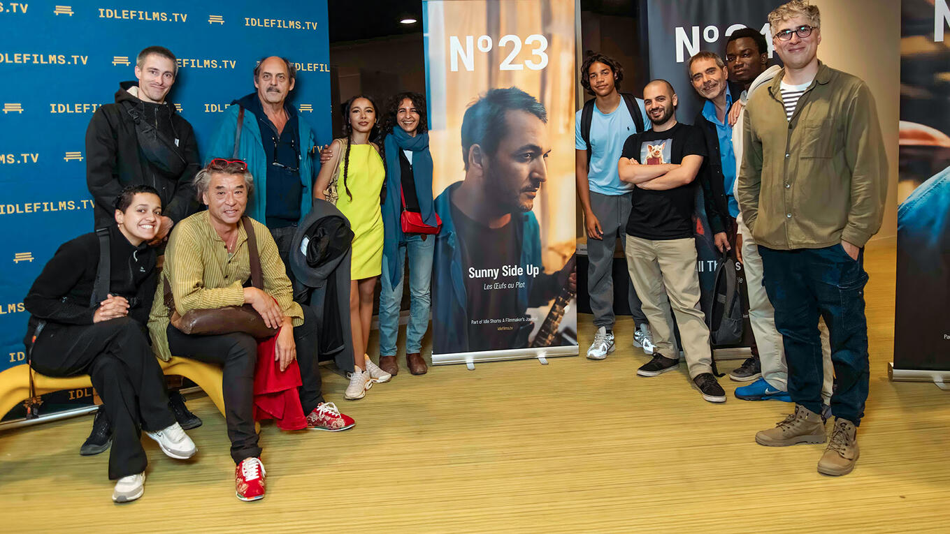 A group photo of around 15 people standing and smiling in front of Sunny Side Up and Idle Films banners, taken at the Marseille screening.