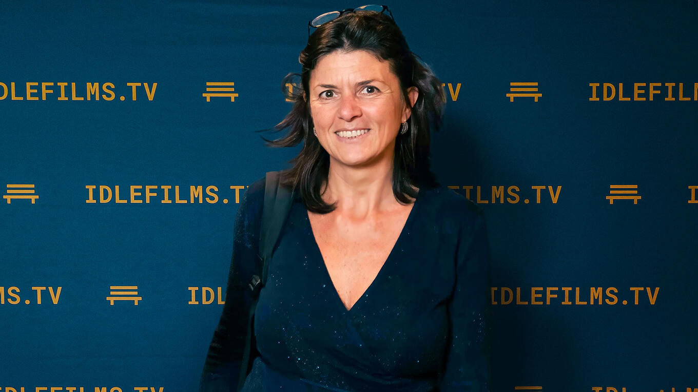 Nathalie Oger smiling in front of the Idle Films step-and-repeat wall, wearing a dark blue top.