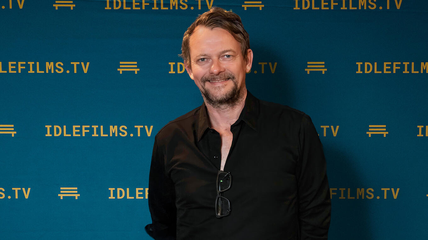 Holger Jaquet smiling in front of the Idle Films backdrop, wearing a black shirt.