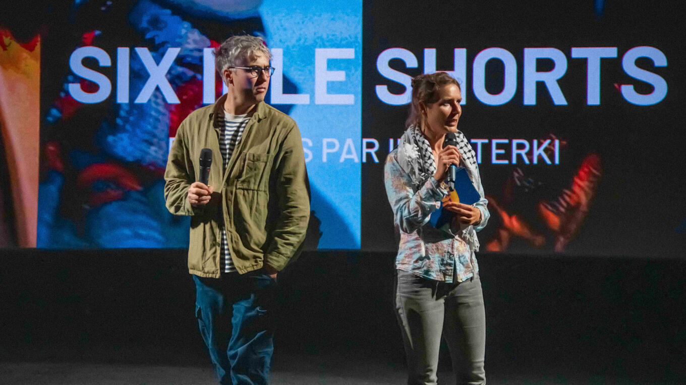 Iliès Terki and Sarah Limorté on stage in front of a large screen reading “Six Idle Shorts” during the Marseille event.