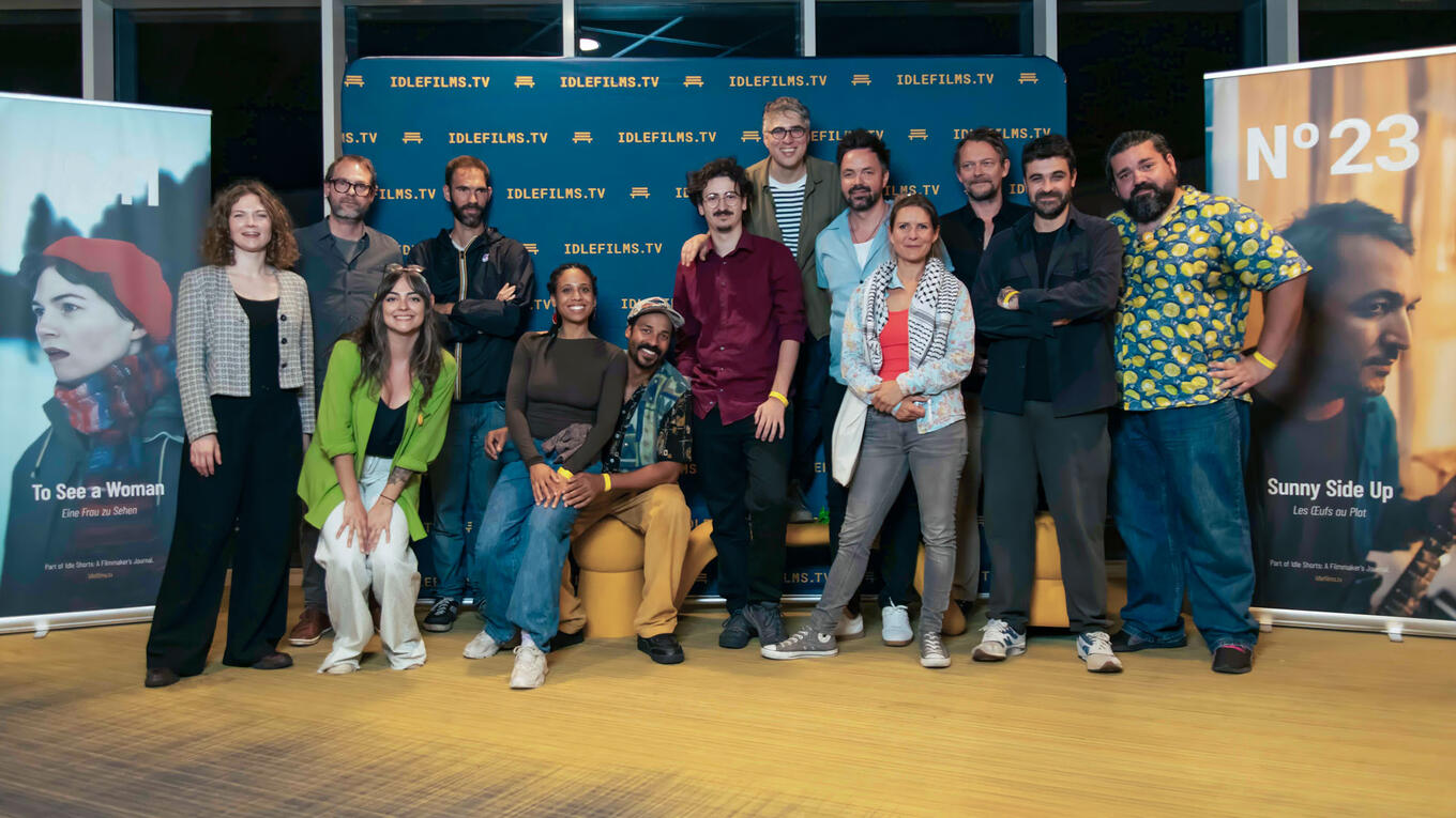 Group photo of Idle Films team and collaborators standing in front of the Idle Films backdrop and posters, smiling after the Marseille screening.