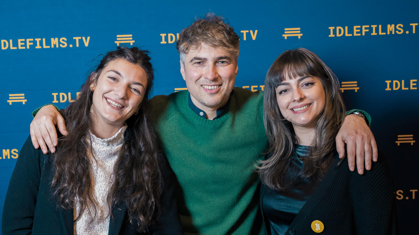 Eva Faure, Iliès Terki, and Gabriela Mais smiling in front of the Idle Films backdrop at the Hamburg premiere.