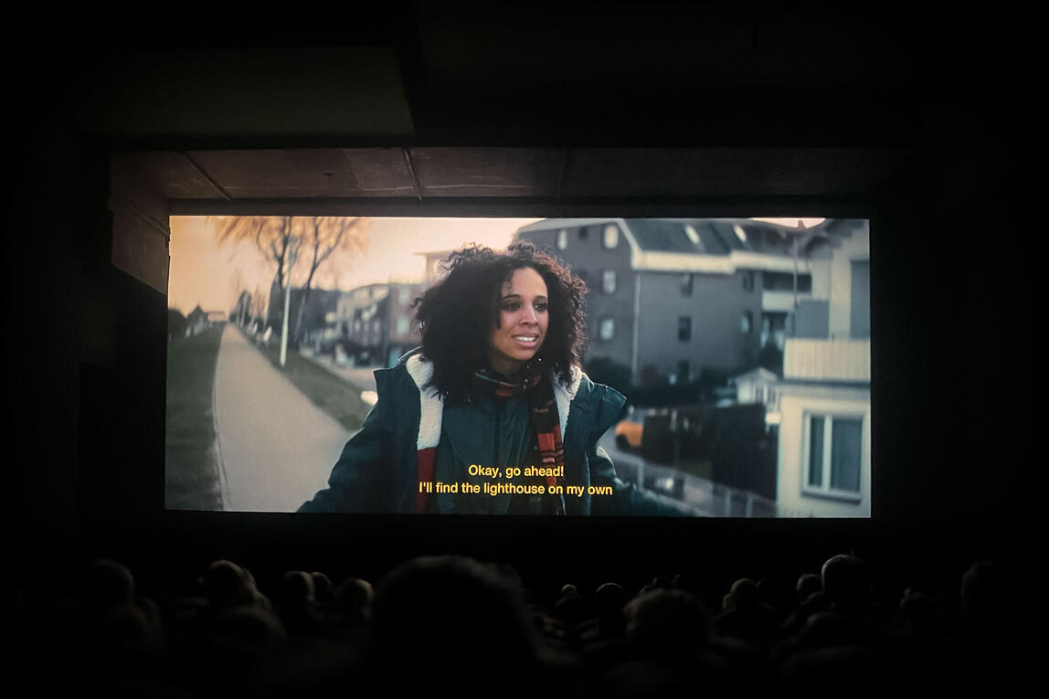 Audience watching a scene from Getting Lost at Moviemento Kino, featuring a woman walking down a path, subtitles visible.